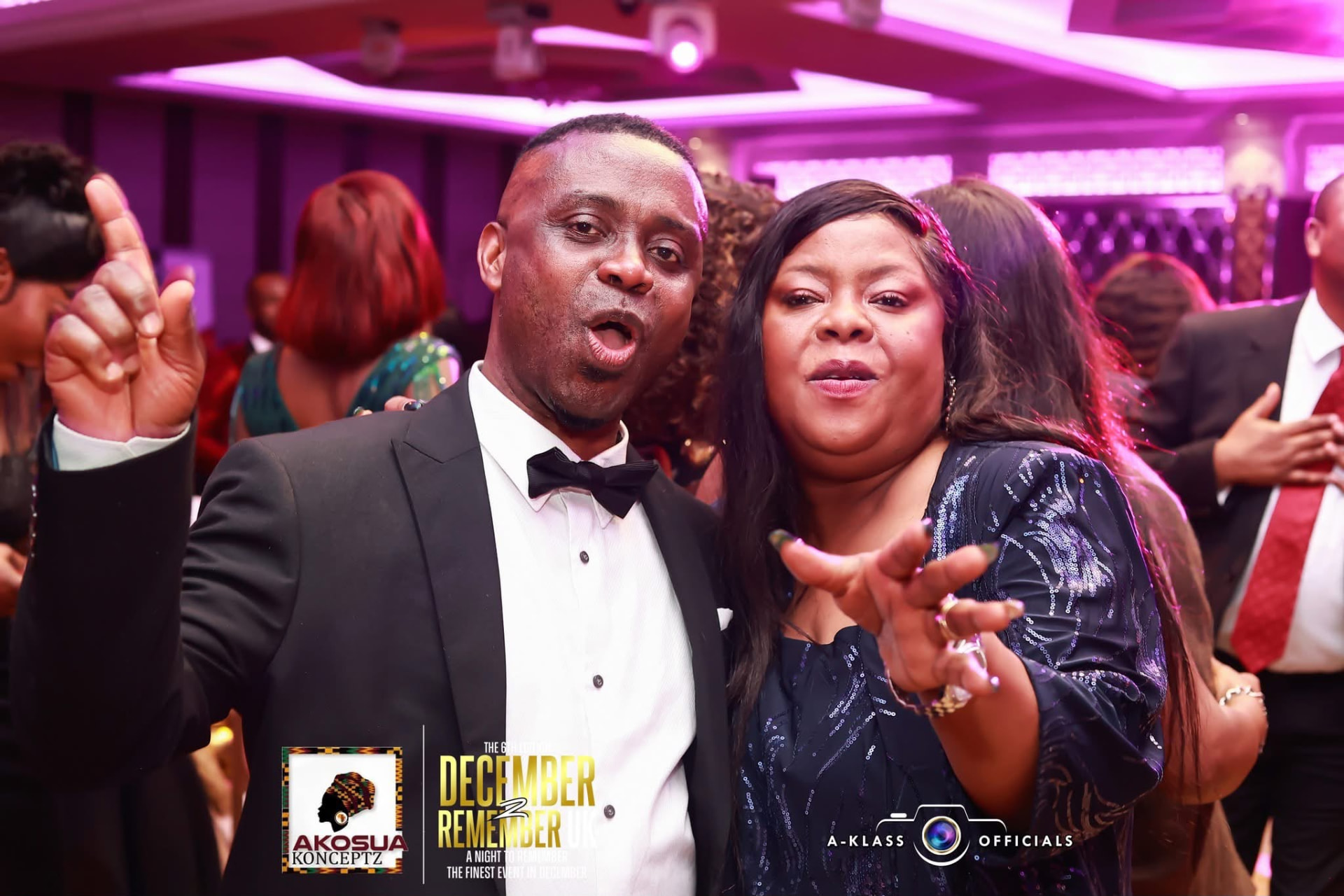 A couple in black tie greeting the camera mid-celebration